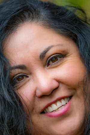 Close-up portrait of a smiling chubby Latin woman face, long black wavy hair, brown eyes, tanned...