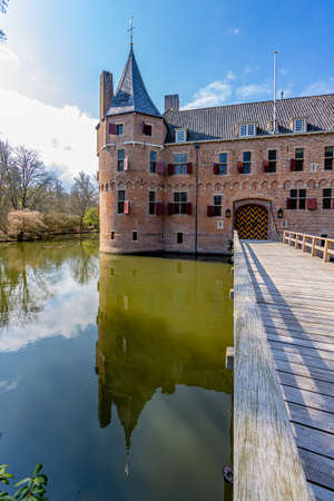 Wooden bridge over the moat with Het Oude Loo castle tower reflected on the water surface, sunny spring day with blue sky and white clouds in Paleispark Kroondomein, Apeldoorn, Netherlandsのeditorial素材