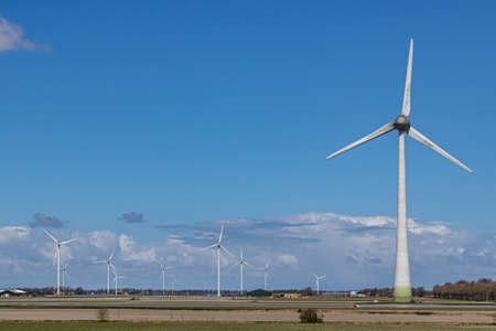 Huge windmills between farmland with farms and trees in the background, sunny day with a blue sky...