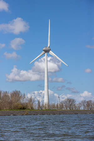 Huge windmill at the seaside with bare trees in the background, sunny day with a nice blue sky and...