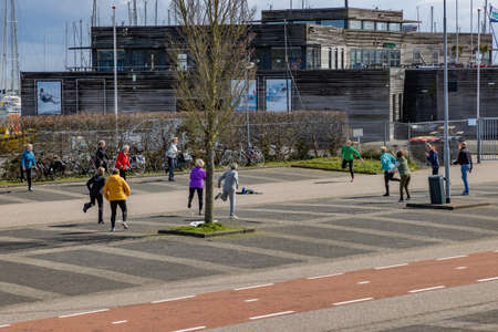 Medemblik, North Holland, Netherlands. April 14, 2021. People in groups of two exercising outside the gym in the parking lot, in coronavirus time, building in the background, quiet and cloudy dayのeditorial素材
