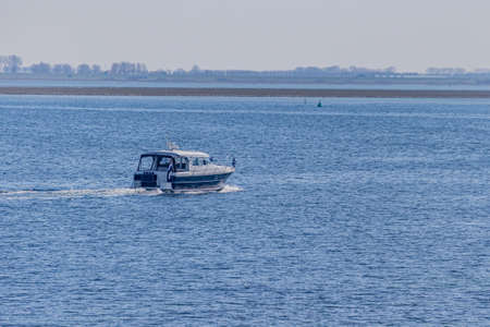 Boat sailing in the calm waters of Lake Grevelingen with the shore with trees in a blurred...