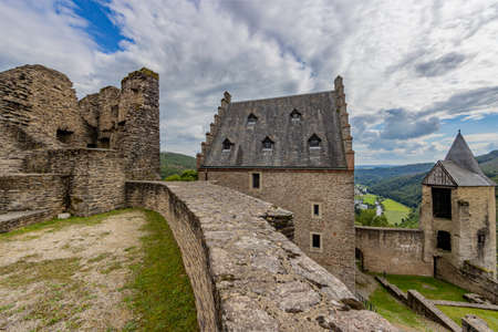 Upper courtyard in the outdoor ruins of the medieval castle of Bourscheid, ruined walls, a building and the watchtower, hills covered with lush green trees in the background, Luxembourgの写真素材