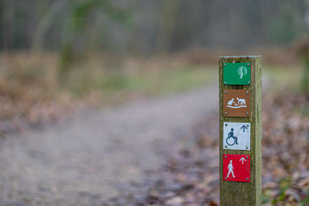 Focused foreground of a hiking trail sign with a path in the background blurred, nature reserve,...