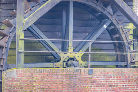 Wooden static water mill wheel with green moss between a wooden wall and a brick wall in the...