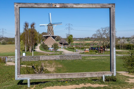 Huge wooden frame on a hill in the Molenplas nature reserve with the Dutch windmill Hompesche Molen in the background, sunny day with a blue sky in Stevensweert, South Limburg, the Netherlandsの写真素材