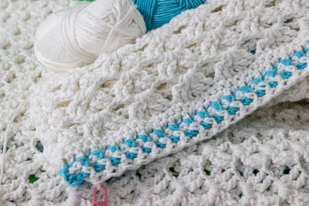 Edge of a white crochet blanket with unfinished blue detail, embossed crochet stitch pattern, pink...