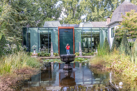 Grathem, South Limburg, Netherlands. September 7, 2022. Garden with a pond and fountain in the old castle of Kasteel Groot Buggenum, photographer taking photos with modern building in the backgroundのeditorial素材