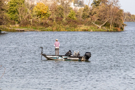 Eijsden, South Limburg, Netherlands. October 28, 2022. Rear view of boat with a fisherman on Lake Grindgat Oost Maarland, along river Maas, seen from Eijsder Beemden Nature Reserve on an autumn dayのeditorial素材