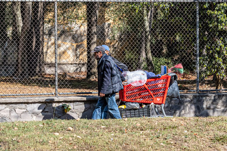 Zapopan, Jalisco Mexico. January 1, 2023. Two homeless Latin American men walking on the sidewalk with their shopping carts full of their belongings, problem in big cities, sunny day in the cityのeditorial素材
