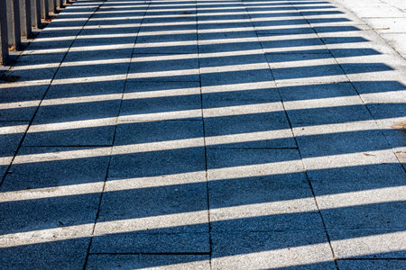 Railing shadows reflected on floor of a pedestrian bridge, over a stream in a Mexican public park on a sunny day, path and grass in the backgroundの写真素材
