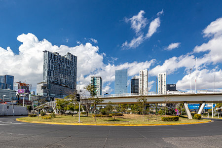 Zapopan, Jalisco Mexico. January 1, 2023. Cityscape with roundabout, elevated vehicular bridge over Acueducto avenue, modern buildings against a blue sky on a sunny day in the backgroundのeditorial素材