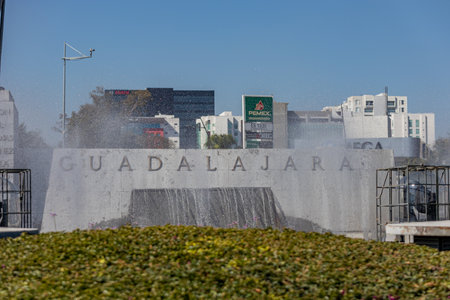 Guadalajara, Jalisco Mexico. January 8, 2023, Wall with inscription: Guadalajara at Glorieta Minerva fountain against blue sky, buildings in background, fountain in operation on sunny day in the cityのeditorial素材