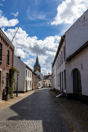 Empty cobbled street between house with white walls, tower of St. Michael's Abbey church in...