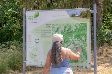 Utscheid, Germany, June 17, 2023. Female tourist checking information board of nature area Naturwanderpark Delux and Eifel Tours, hiking routes, distances, topography and place informationのeditorial素材