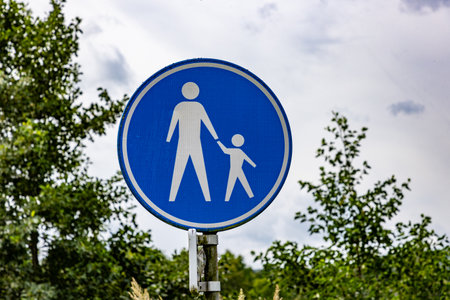 Pedestrian route or walking area sign against cloud covered sky and green foliage in background,...