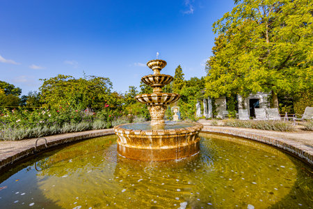 Old baroque fountain with round pond, green leafy trees against blue sky in background, sunny spring day in gardens of Arcen Castle, Limburg, Netherlandsの写真素材