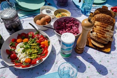 Picnic table with variety of food, Mediterranean salads, boiled eggs, jam and bread, lunch outdoors on garden terrace, enjoying a sunny summer dayの写真素材