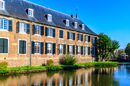 Brick wall with multiple windows and gable roof of Wijnandsrade Castle surrounded by its moat,...