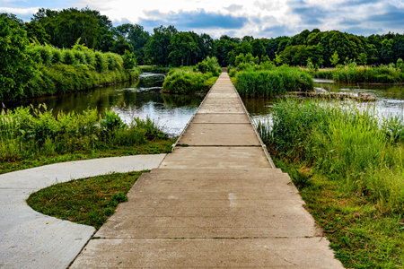 Landscape of Kapermolen Park with pedestrian path over water between Demer River and tributary pond, calm water, and leafy trees around and in background, Hasselt, Belgiumの写真素材