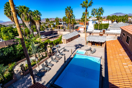 Top view of villa sunbathing area with a pool, sun loungers, palm trees, houses, buildings and mountains against blue sky in background, sunny spring day in Loreto, Mexicoの写真素材