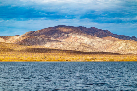 Arid landscape of Mexican coastal shoreline, beach, meadow and mountain range against blue sky, dry and yellowish wild grass, Loreto in Baja California Sur, Mexicoの写真素材