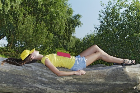 The girl fell asleep with the book  Lying on a fallen tree  Sunny Dayの写真素材