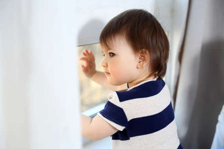 Beautiful baby girl is looking through the windowの写真素材