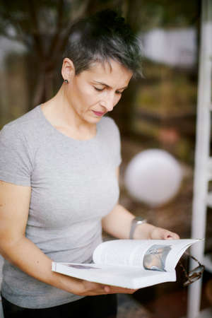 Lady in short shirt, concentrating with an open book and a pair of glasses in her hands