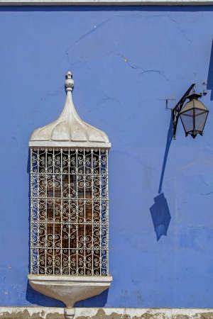 Antique window with bars on a colorful wall and a street lamp hanging from the wall casting a...