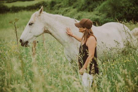 A woman in a meadow with tall grass petting a white horse.の写真素材