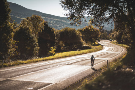 A woman cyclist training on a lonely road on a sunny day wearing a black jersey and bib shorts and a white helmet.の写真素材
