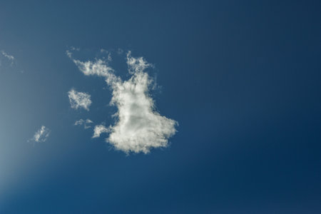 The image depicts a serene and expansive sky filled with a variety of fluffy, white clouds against a...