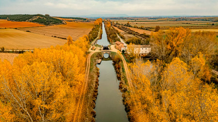 erial View of Canal de Castilla in Autumn, Palencia. Aerial shot of Canal de Castilla in Palencia, Spain, lined with golden autumn trees, fields, and historic buildings, showcasingの写真素材