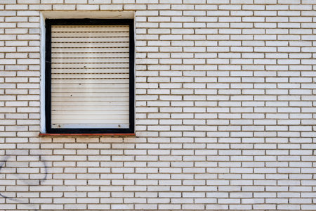 A minimalistic design of a white brick wall featuring a single closed window with shutters, creating...