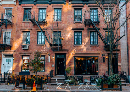 A cozy brick building with fire escapes, storefronts, and outdoor seating in a quiet New York City street, capturing urban charm and character.の写真素材