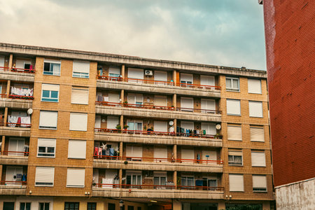 A brick apartment building with multiple balconies, some adorned with drying laundry, under a cloudy sky. Captures urban lifestyle and daily routines.の写真素材