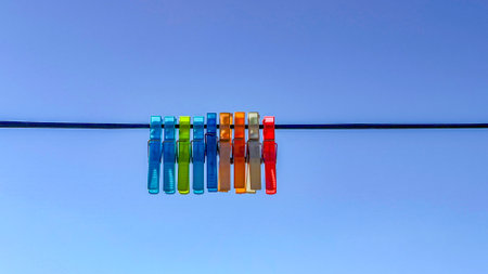 Brightly colored clothespins hang on a line. The vivid contrast between everyday objects and nature...