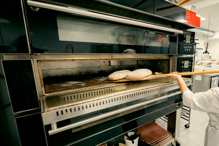 Freshly baked bread being removed from a modern professional oven in a bakery. Artisan baking...