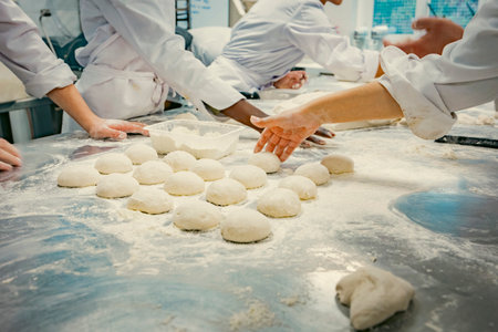 Hands of baking students working with fresh dough in a professional kitchen. Artisan bread preparation, teamwork, and pastry training in a culinary school. Flour, dough balls, and rolling techniques.の写真素材