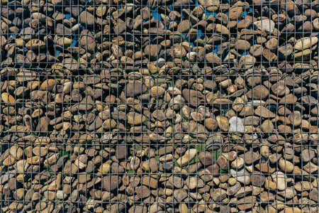 Close-up of a gabion wall made of smooth river stones encased in a metal wire grid. Earthy textures and geometric pattern ideal for architectural or design use.の写真素材
