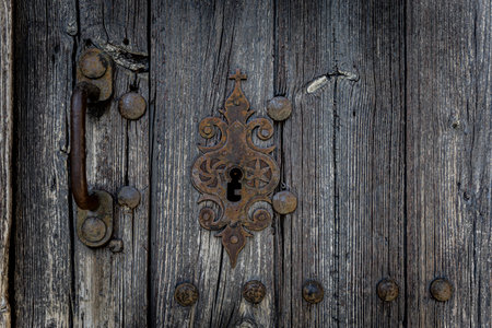 Close-up of an old weathered wooden door with an ornate rusted metal lock and textured grain. Vintage, rustic detail with strong character and patina.の写真素材