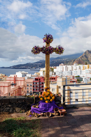 Symbolic bamboo cross decorated with vibrant flowers and cloth, placed on a stone wall with a scenic urban and coastal backdrop.の写真素材
