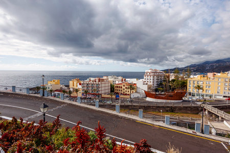 Elevated panoramic view of a coastal town in La Palma with vibrant buildings, mountain backdrop and Atlantic Ocean under dramatic clouds.の写真素材