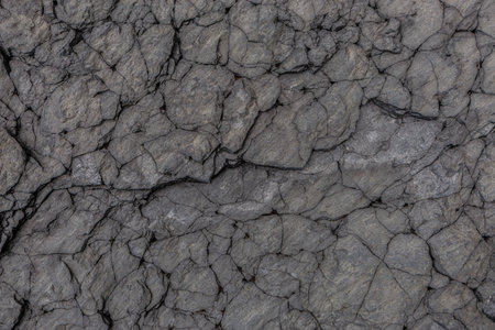 Detailed close-up of fractured volcanic stone surface with natural crevices and layered textures,...
