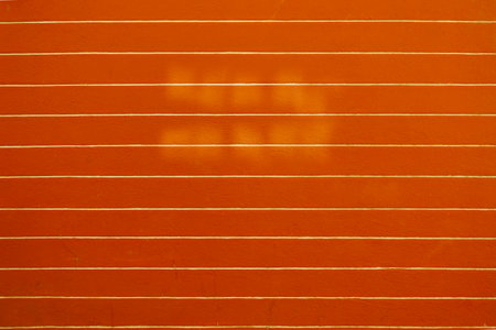 Geometric background of a vivid orange wall featuring evenly spaced white stripes and soft shadow textures, ideal for design and abstract use.の写真素材