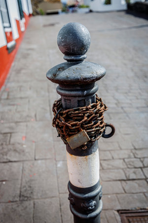 Close-up of an old metal post wrapped in a corroded chain and padlock, evoking feelings of limitation, control, and psychological restraint.の写真素材
