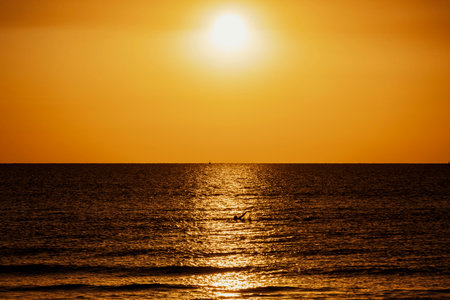 A tranquil morning scene of a person swimming through glowing reflections of the rising sun on the Mediterranean waters off the coast of Cyprus.の写真素材