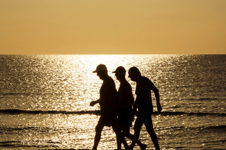 Active older adults enjoy a quiet morning on the Mediterranean coast, walking or bathing during a peaceful golden sunrise in Cyprus.の写真素材
