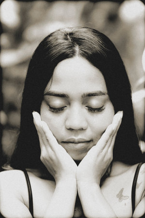 Monochrome close-up capturing a serene yet expressive mood as a young woman gently holds her face,...